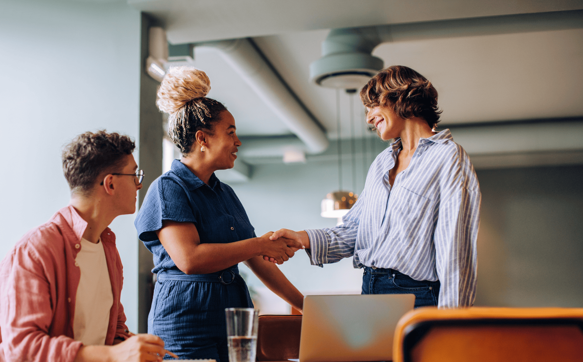Three individuals interact in a professional setting, with one extending a handshake during their discussion