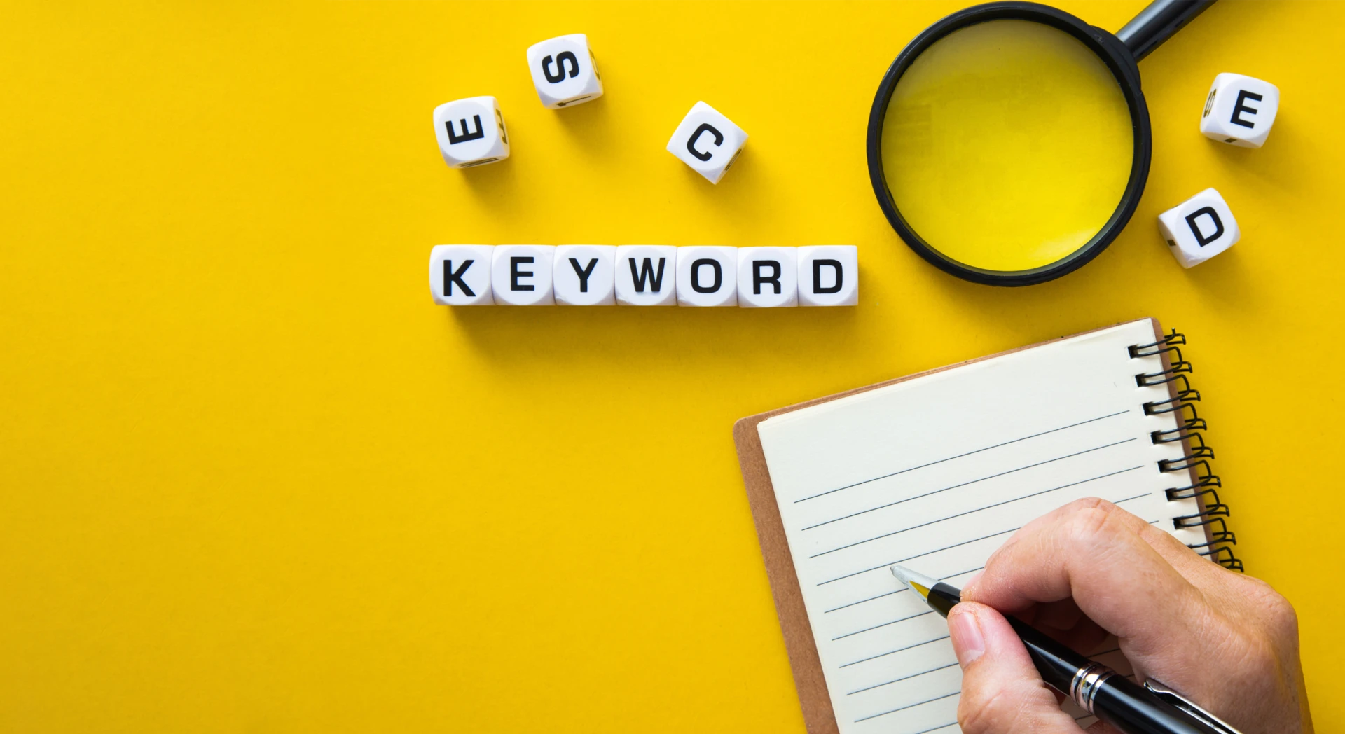 Blocks spelling “keyword” and a hand with a pen writing in a notebook