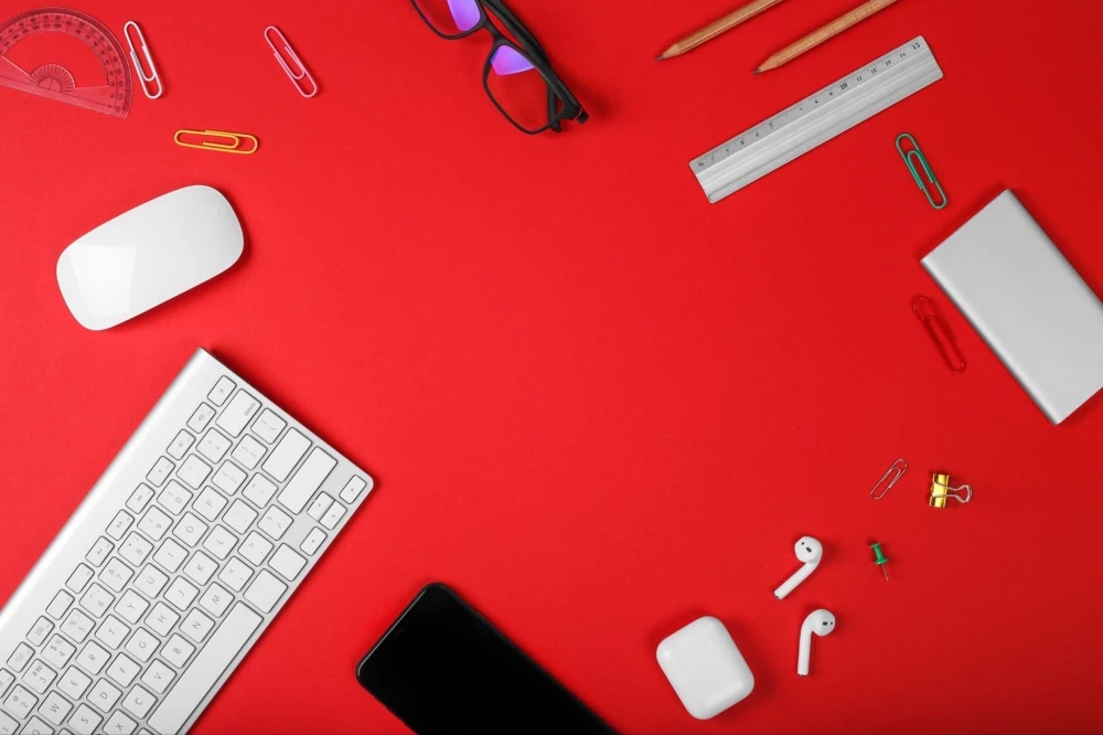 Desk flat lay on red with keyboard, mouse, phone, and earbuds, used for a guide to social media management tools.