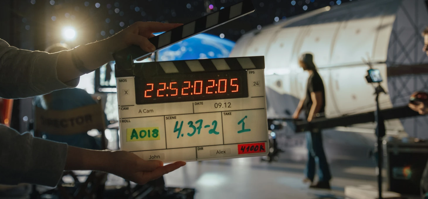 Film crew member holding a clapperboard on a professional video production set with lighting and camera equipment.