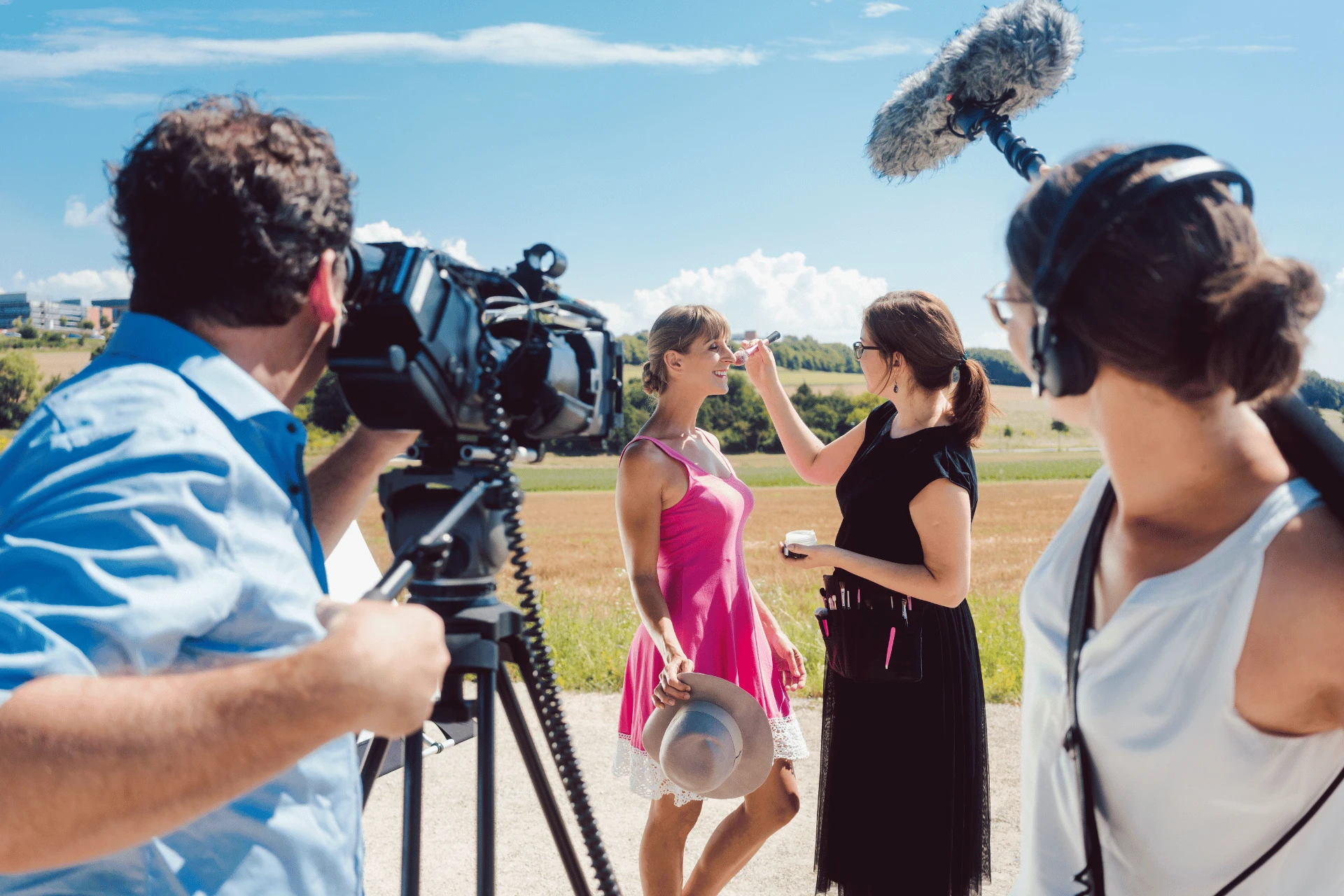 makeup artist touching up an actress's makeup in front of a film crew while shooting outdoors
