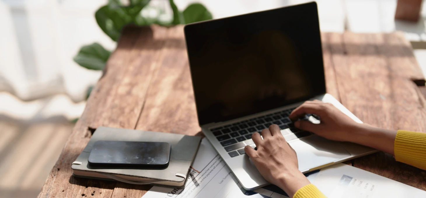 Marketer working at a desk with a laptop, phone, and printed data reports 