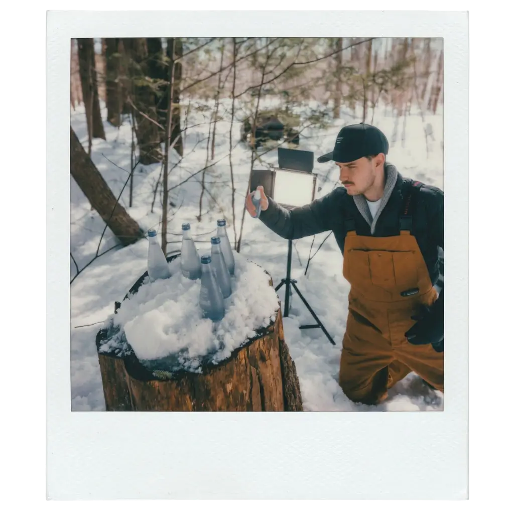 Alister videographer styling sparkling water bottles on a snowy tree stump during an early brand video shoot in the woods