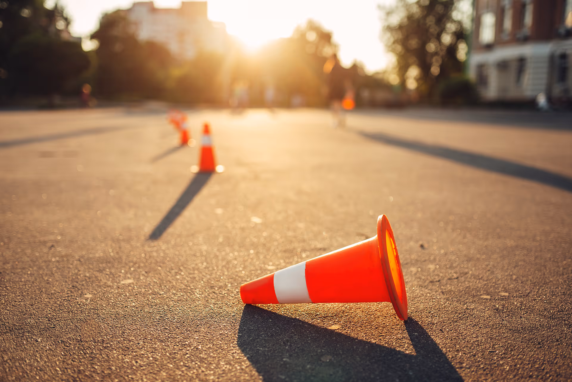 Orange traffic cone lying on street at sunset with long shadows