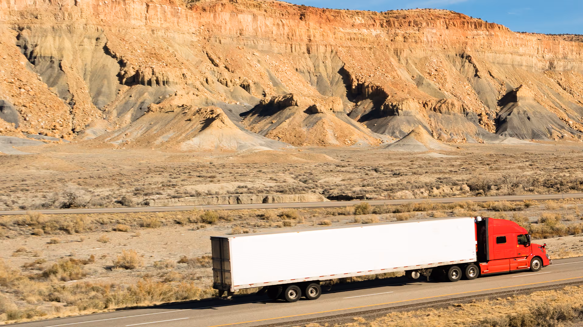 Red semi-truck driving on highway through rocky desert landscape