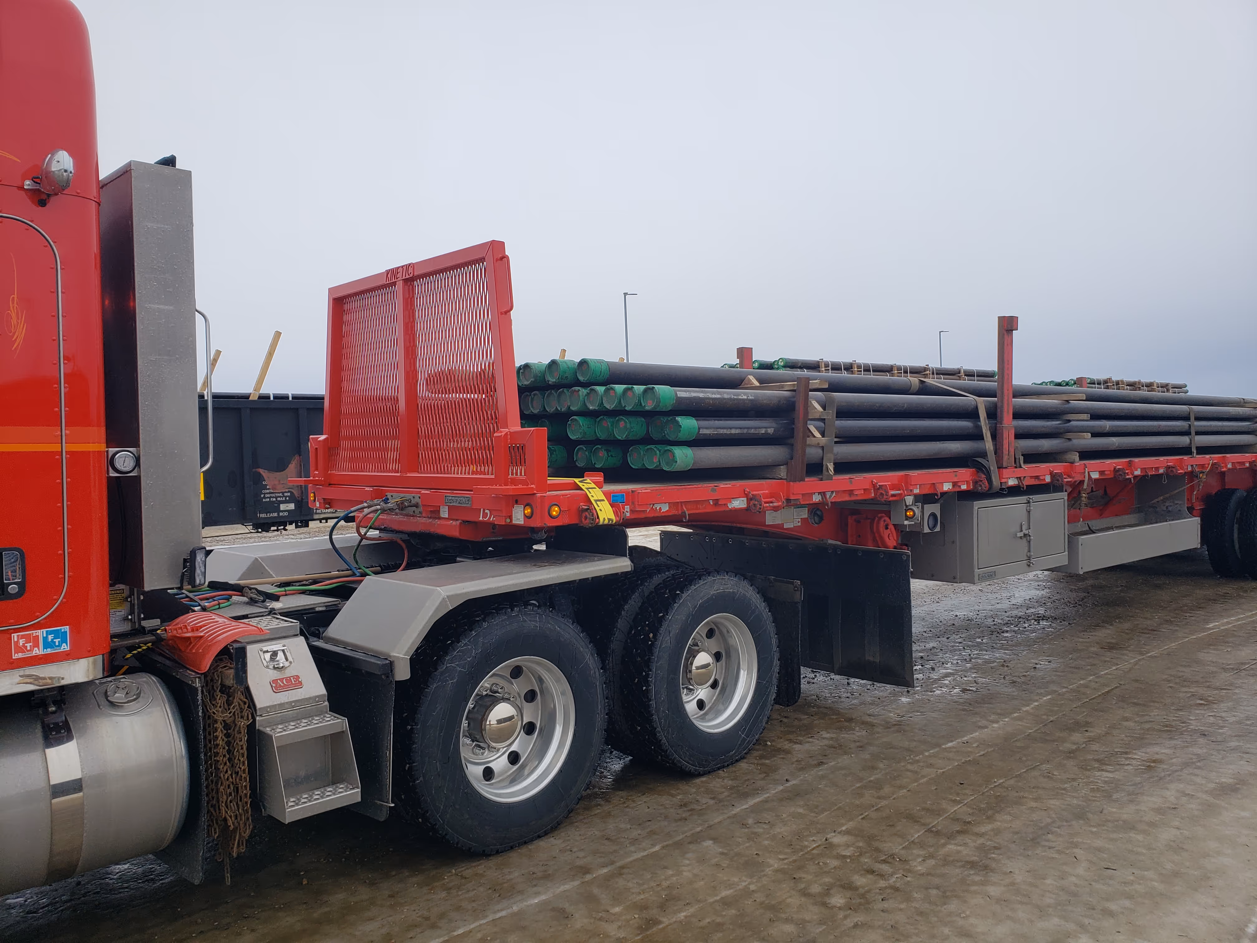 Red truck with flatbed trailer carrying green pipe loads in industrial yard