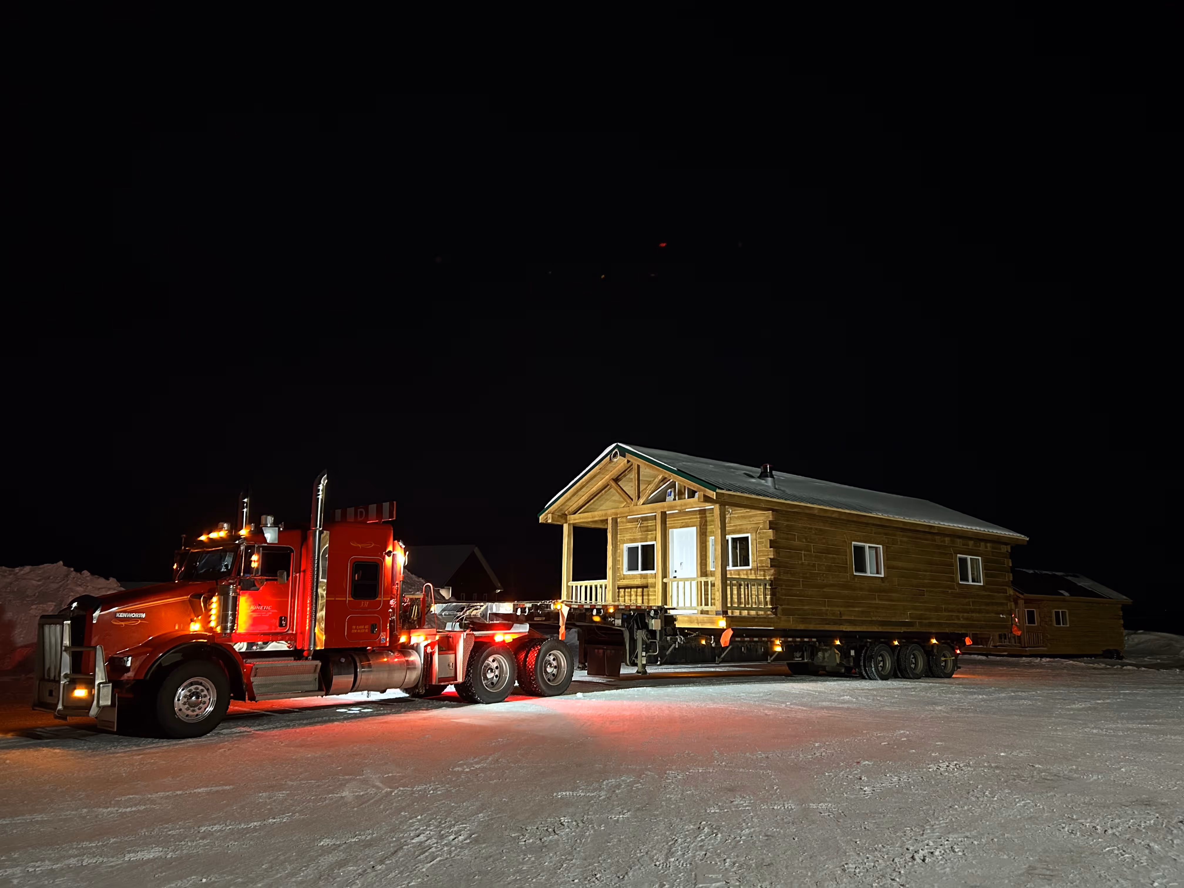 Red truck hauling wooden house at night on snowy ground