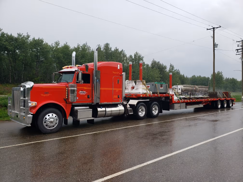 Bright red semi-truck with long flatbed trailer parked on wet road