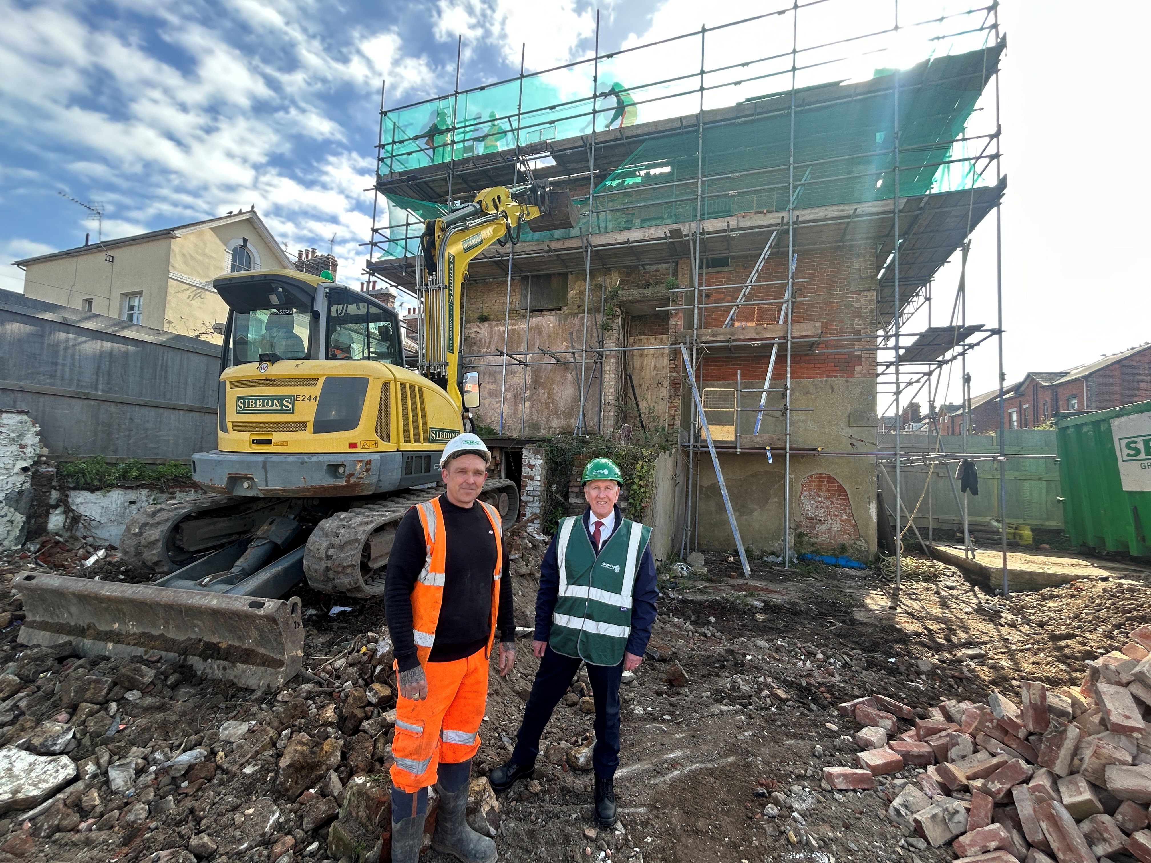Two men with hi vis and hard hats on top of a building