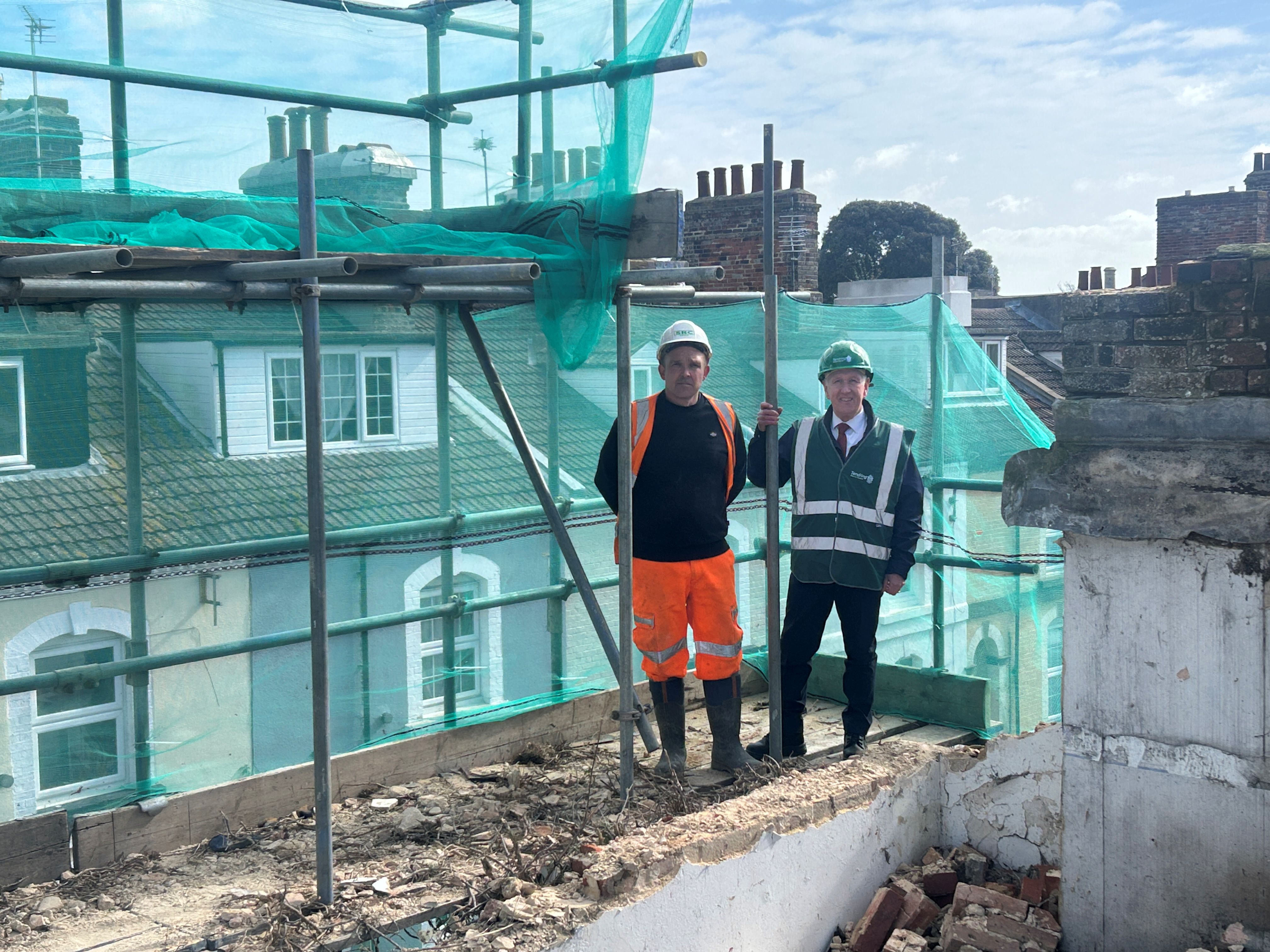 Two men in hi vis and hard hats on top of a building