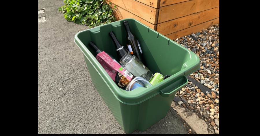 Green box with empty glass bottles and juice cartons in