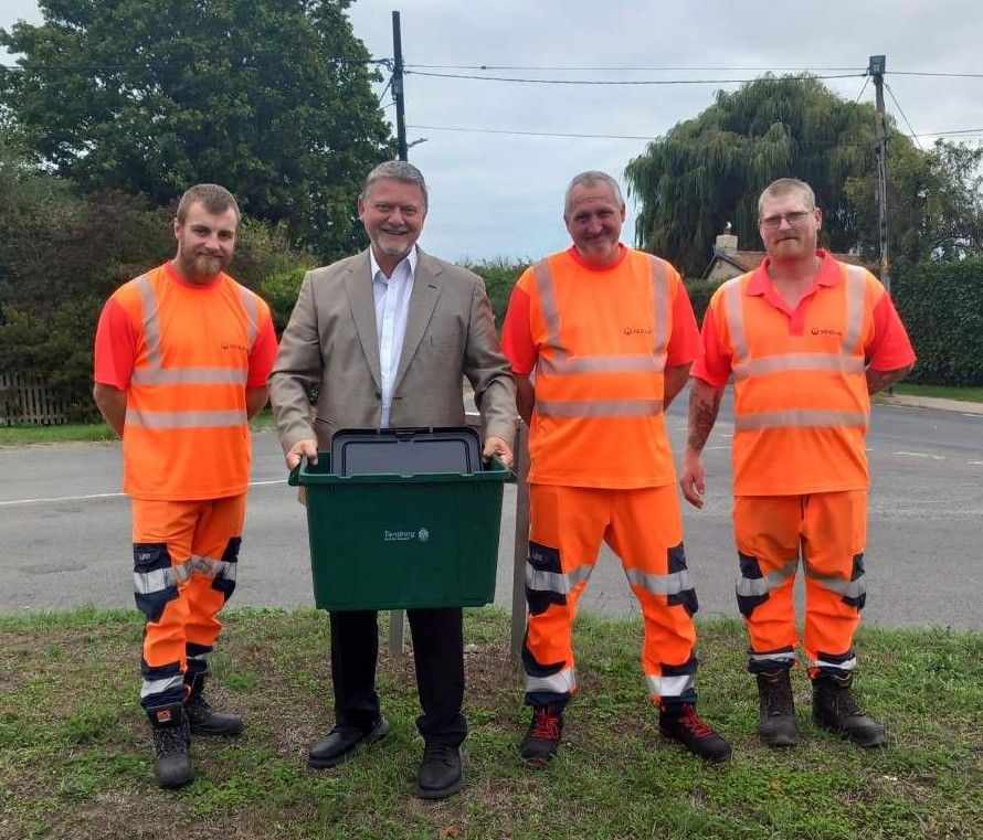 Orange hi-viz bin crew with suited man holding green box