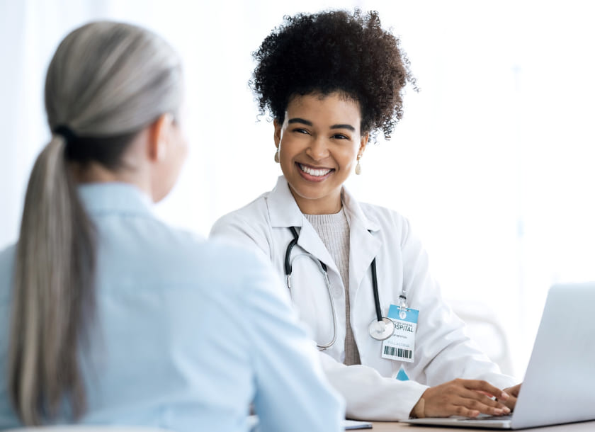 Médica sorridente conversando com paciente em consultório moderno com laptop
