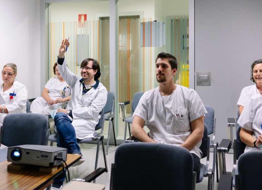 Profissionais de saúde em sala de aula participando de treinamento, com um homem levantando a mão