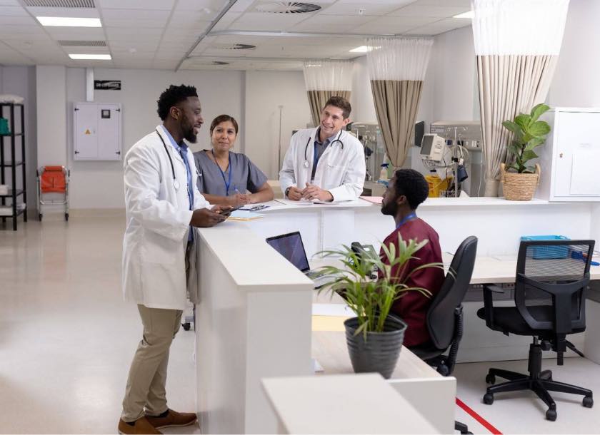 Equipe médica multidisciplinar conversando na recepção do hospital com computadores e plantas decorativas