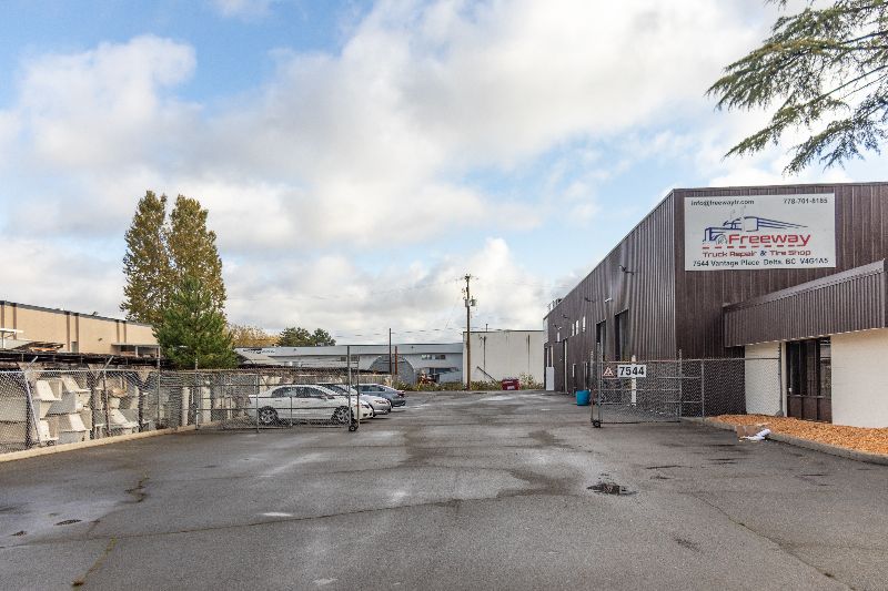 Exterior view of Freeway Truck Repair shop in Delta, BC, showing parking lot, fenced area, surrounding buildings, and cloudy sky.