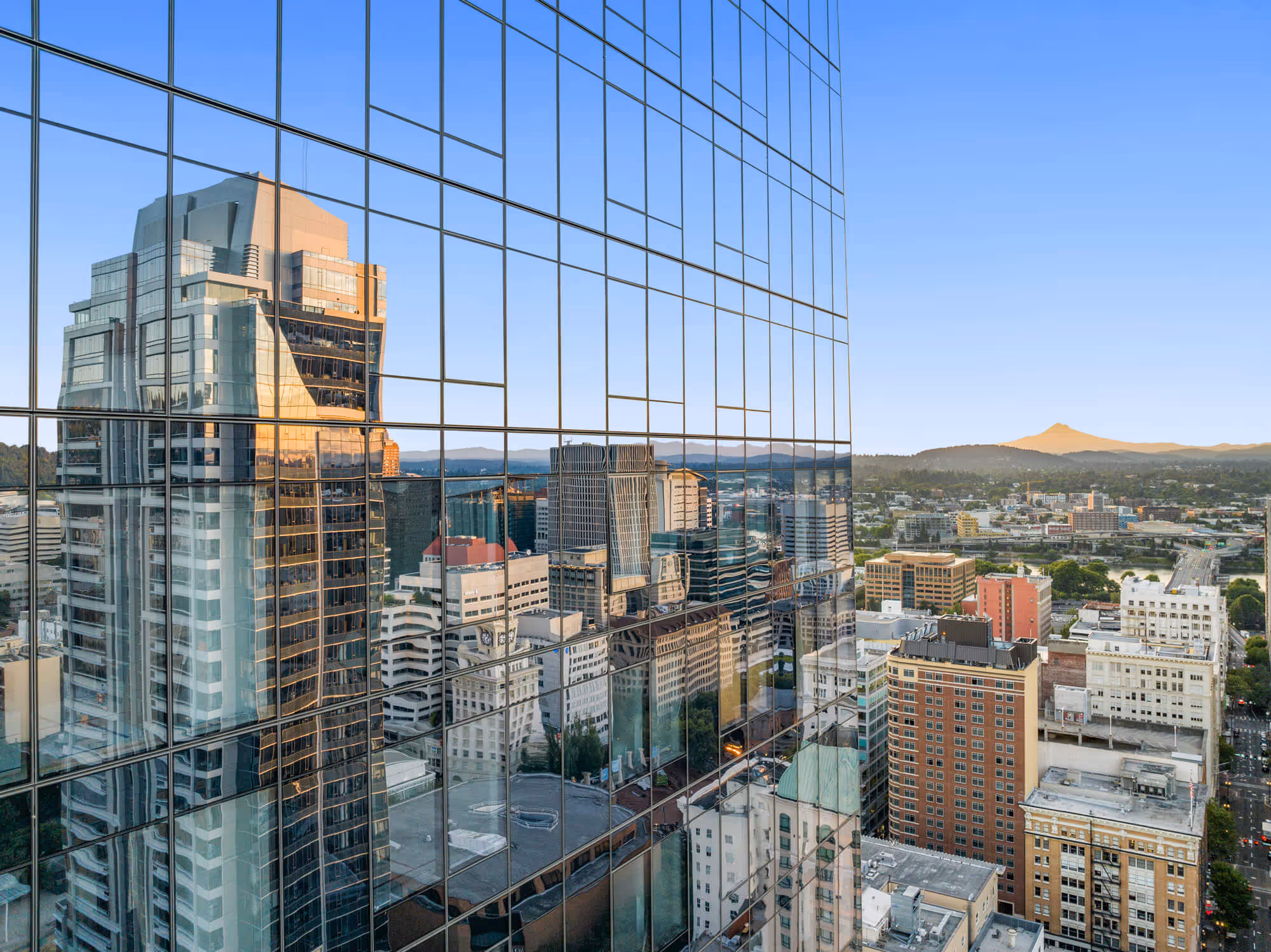 The Portland skyline reflected in Block 216's glass facade with Mt Hood on the horizon