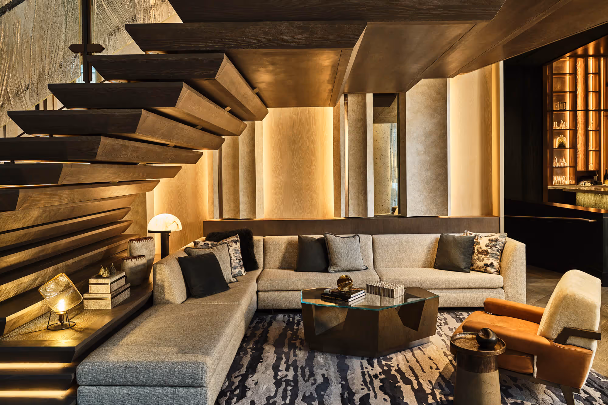 Modern seating with a large gray sectional sofa, geometric coffee table, brown armchair with white cushion, and tucked under the Grand Staircase in The Ritz-Carlton, Portland hotel.