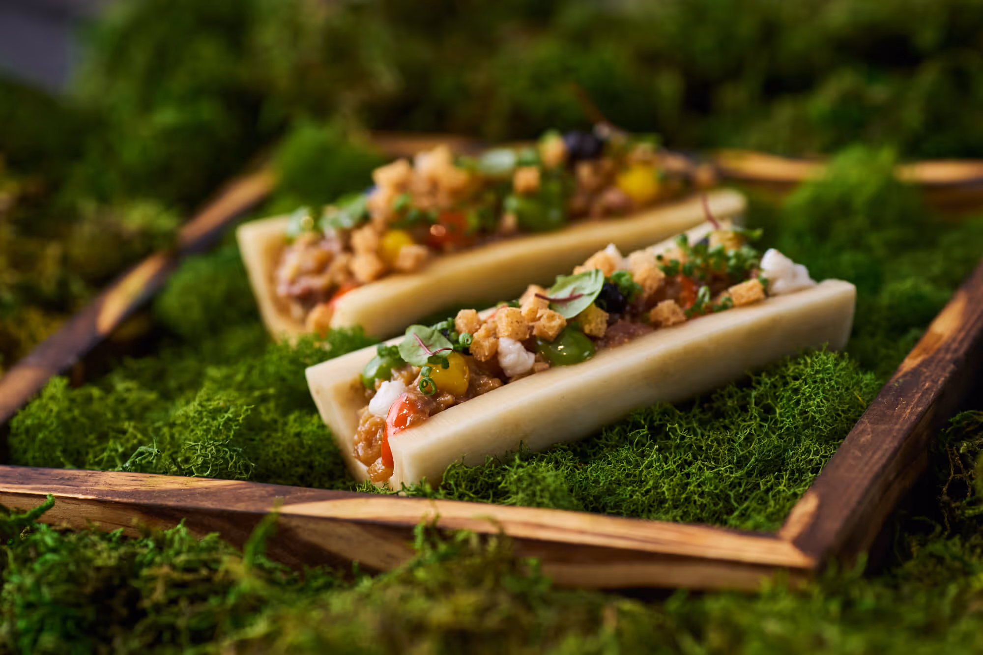 Two gourmet bone marrow appetizers topped with herbs, croutons, and sauces served on a bed of green moss in a wooden tray at Bellpine