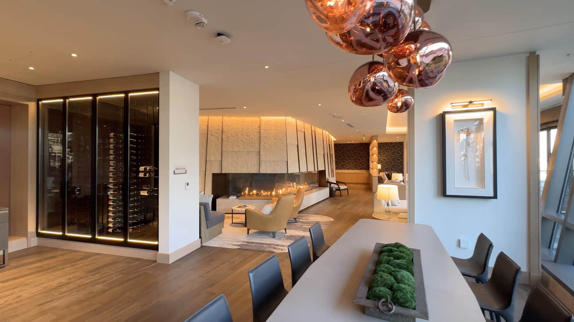 Exclusive Owners' Lounge with a long table, black chairs, hanging copper lights, a large fireplace, and a glass-enclosed wine cellar.
