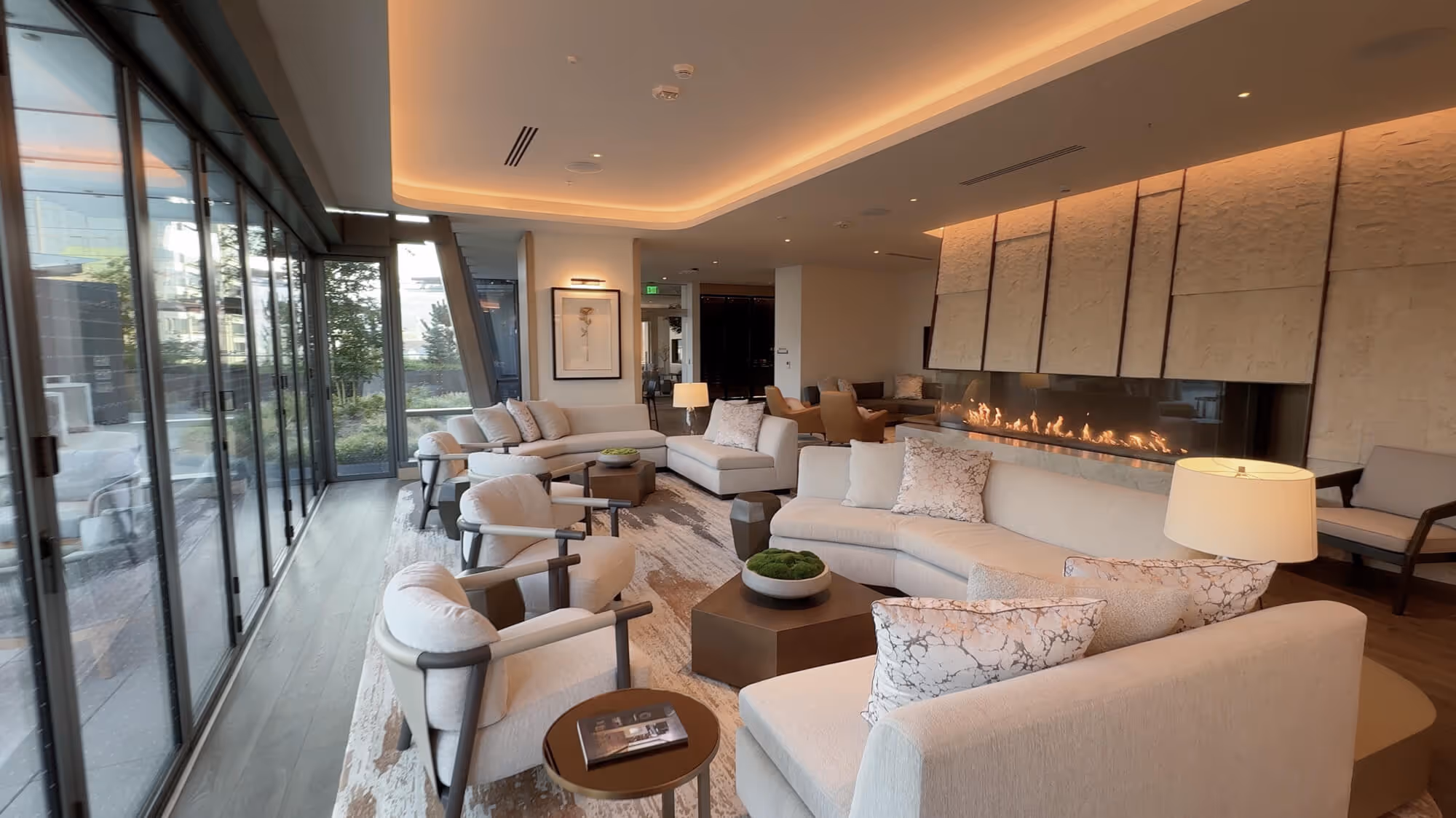 Exclusive Owners' Lounge with beige sofas and armchairs around a low table, featuring a long linear fireplace and large glass windows.