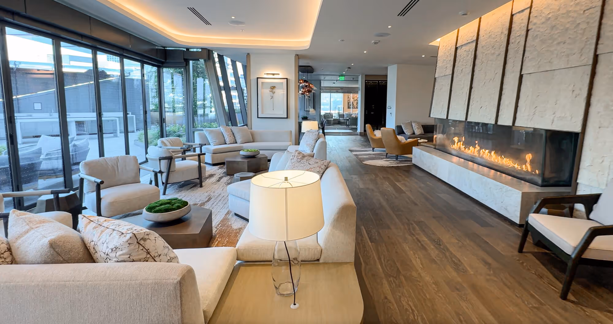 Exclusive Owners' Lounge with beige sofas and armchairs around a low table, featuring a long linear fireplace and large glass windows.