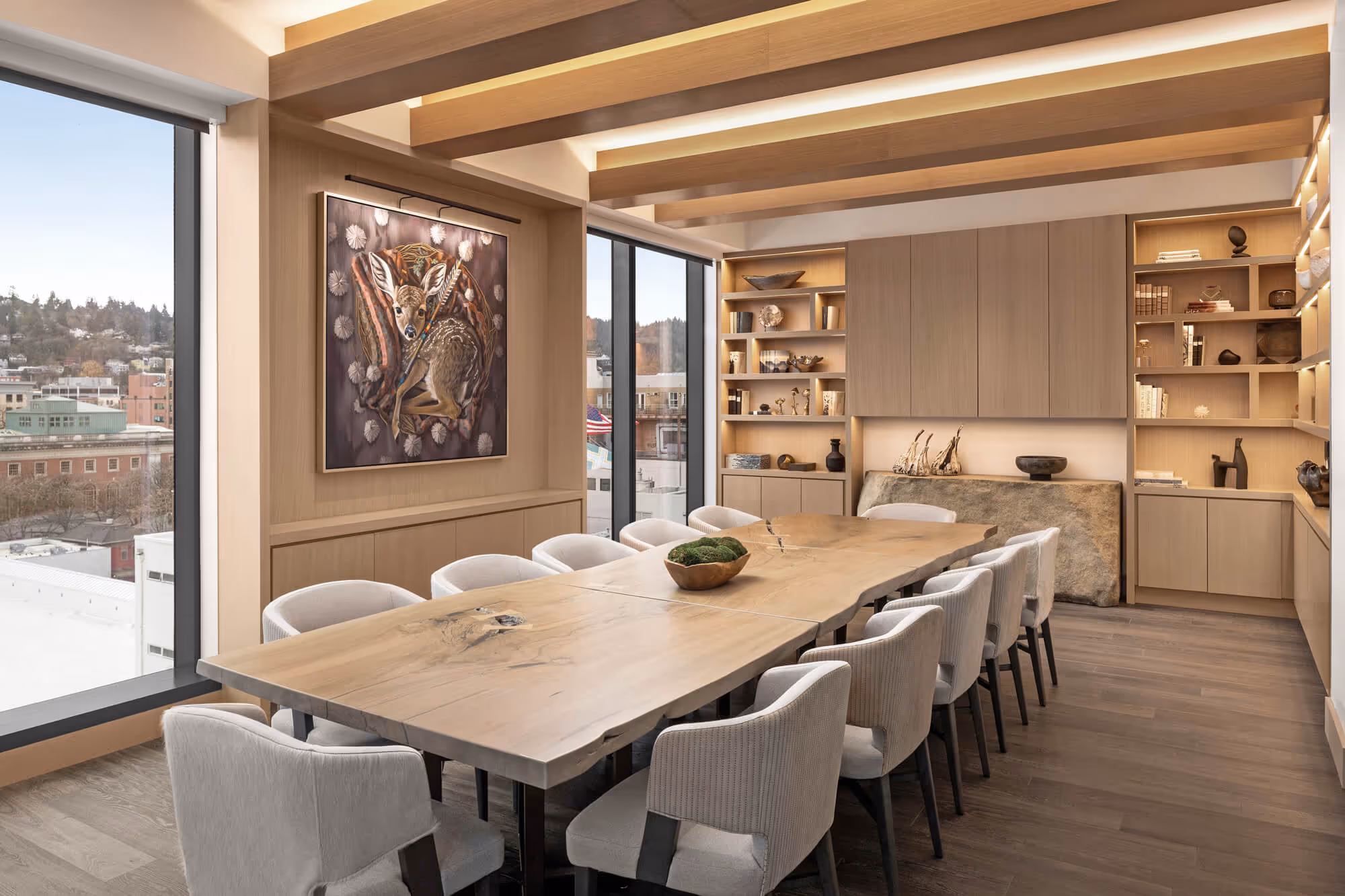 Executive Boardroom in the Exclusive Owners' Lounge with a long wooden table, twelve upholstered chairs, built-in shelves and cabinets, and a large deer painting on the wall.