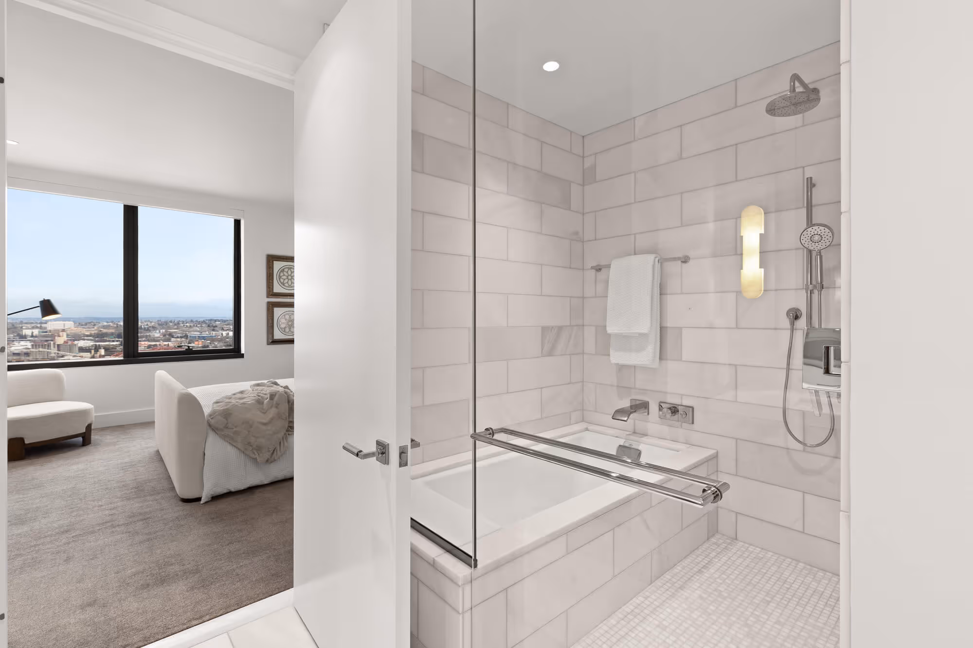 Modern bathroom  at The Ritz-Carlton Residences, Portland with a built-in bathtub and shower, tiled walls, white towels, and a partial view into a bedroom with the Portland cityscape through the window.