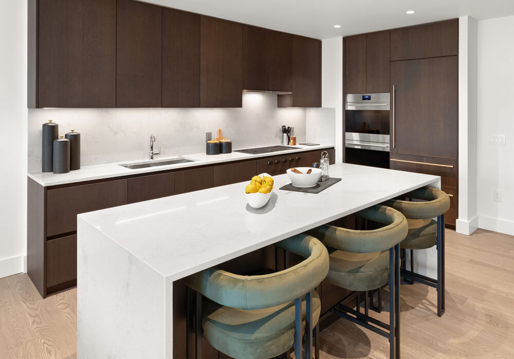 A kitchen at The Ritz-Carlton Residences, Portland showing the Mountain Palette finishes with dark wood cabinets, grey quartzite countertops, and light-stained white oak hardwood floors.