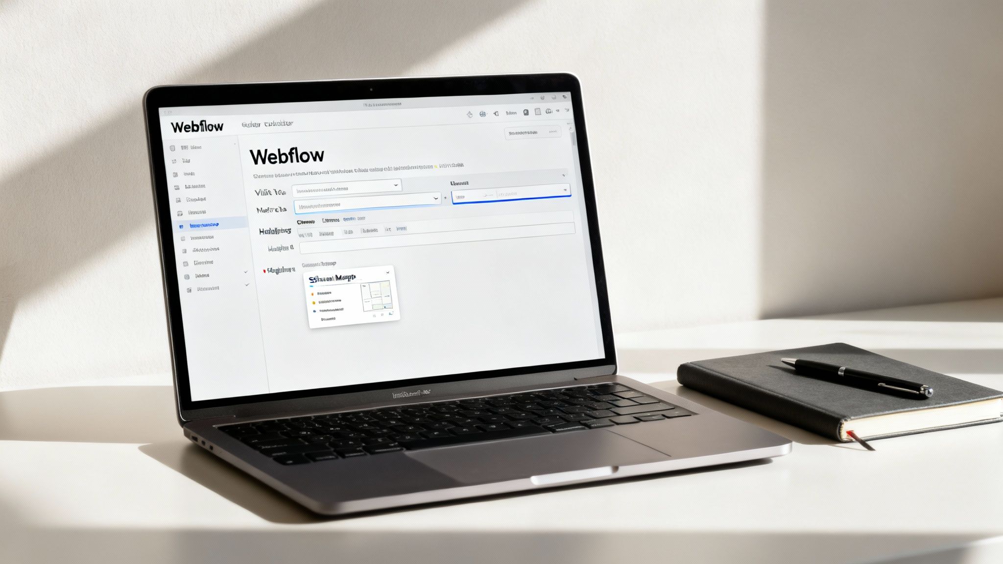A MacBook Pro displaying the Webflow interface with a notebook and pen on a white desk.