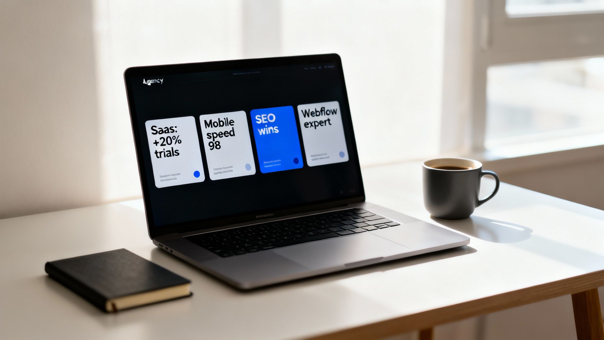 A laptop displaying a digital agency website with service cards, next to a coffee mug and notebook.
