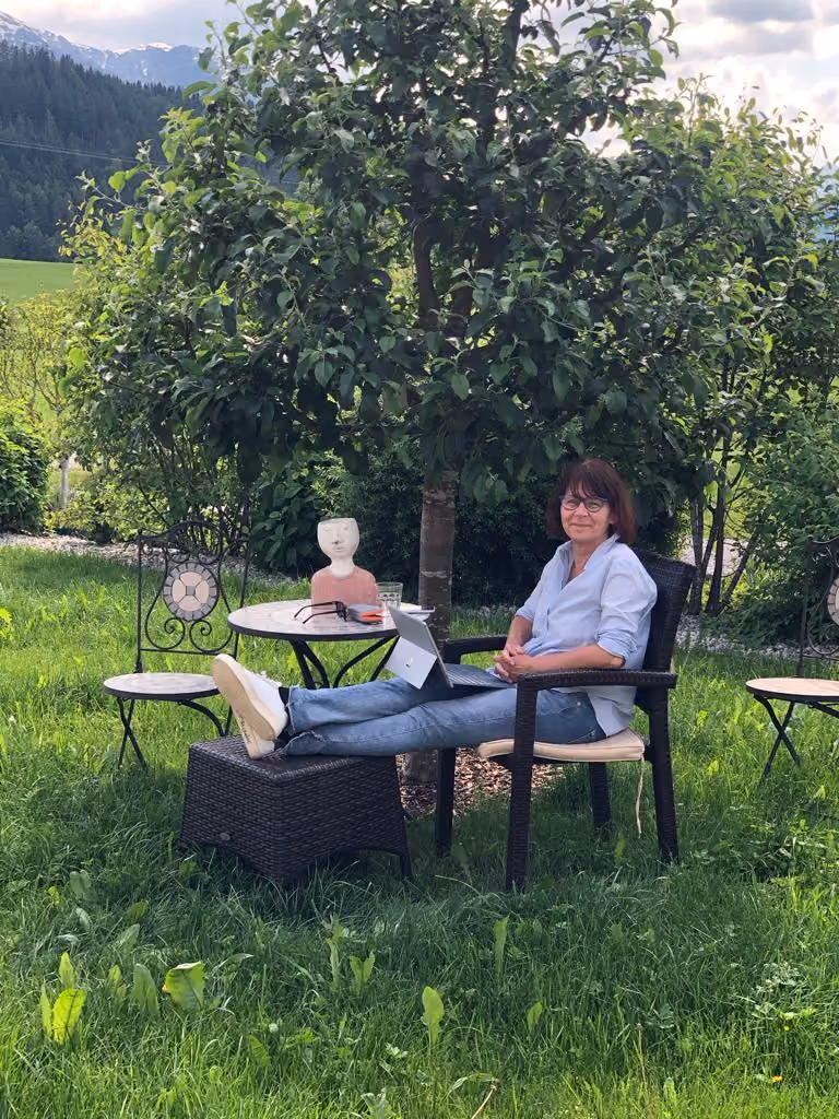 Sabine Steinbeck sitzt mit hochgelegten Füßen im Grünen neben einem geöffneten Laptop.