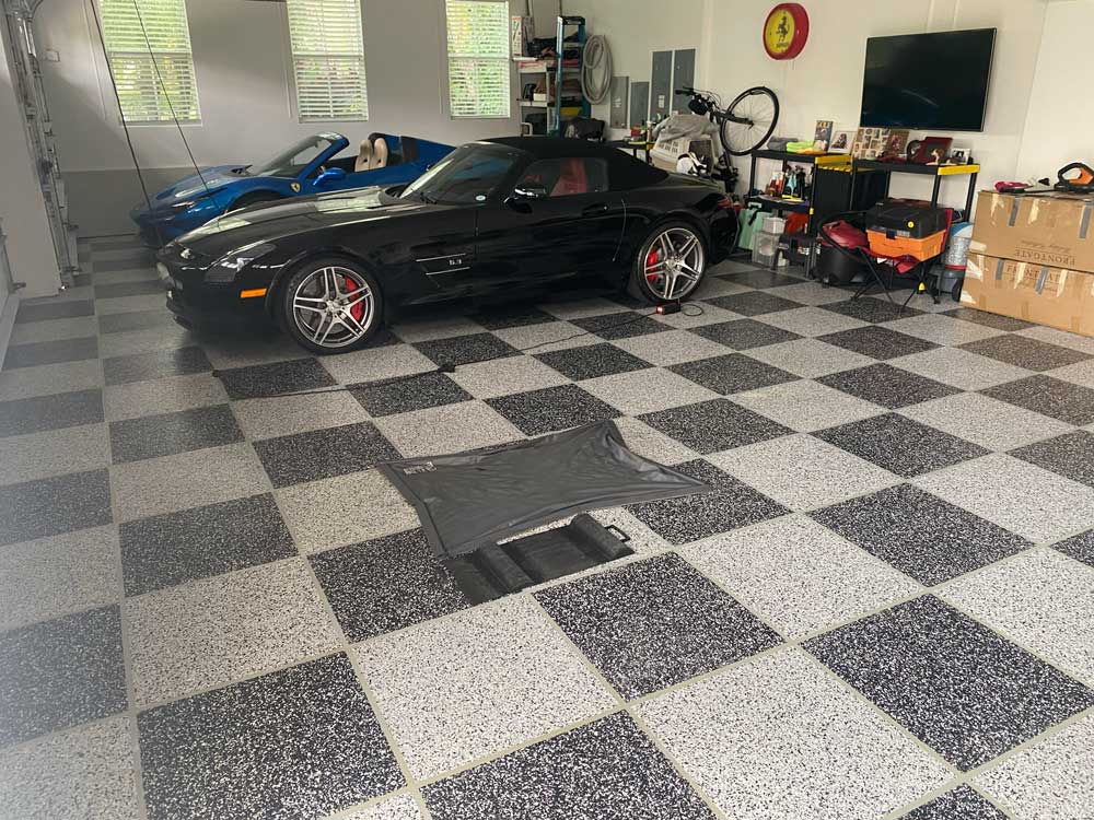 Garage with black and white tiles on the floor and two cars parked inside.