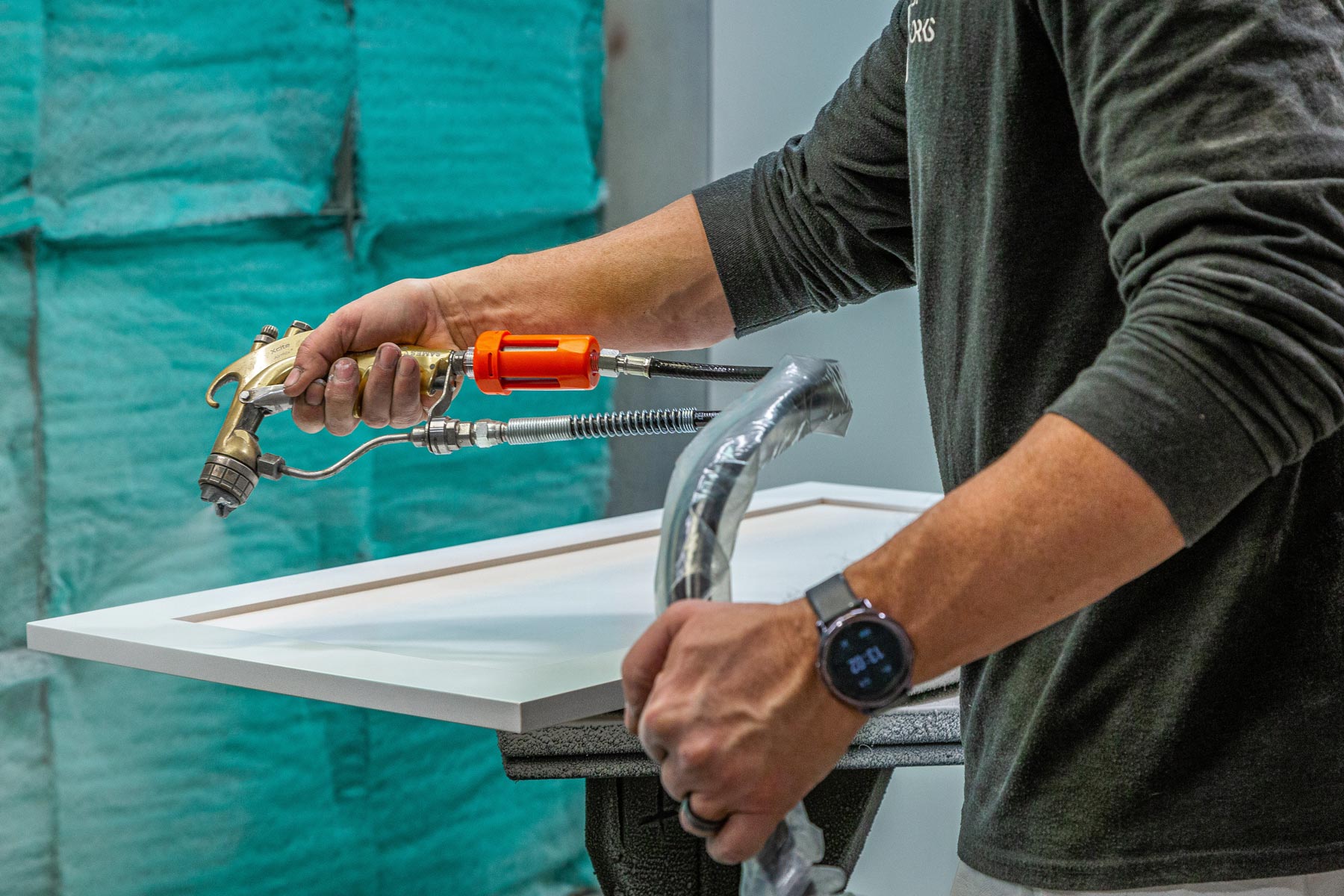 A carpenter spraying finish on a cabinet door.