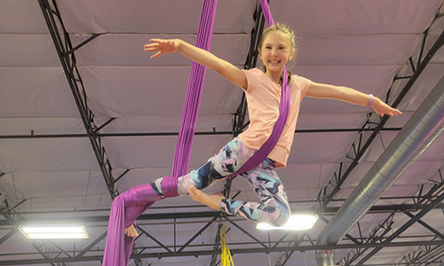 A gymnast suspended by aerial silks with her arms open like a bird.