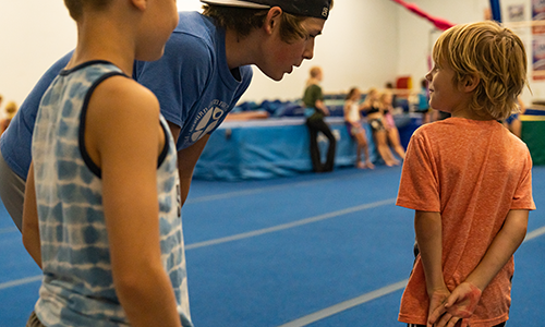 A gymnastics coach leaning over and talking to two young gymnasts.