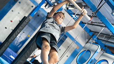 A young boy swinging on a bar on an obstacle course at Auburn Gymnastics Center.