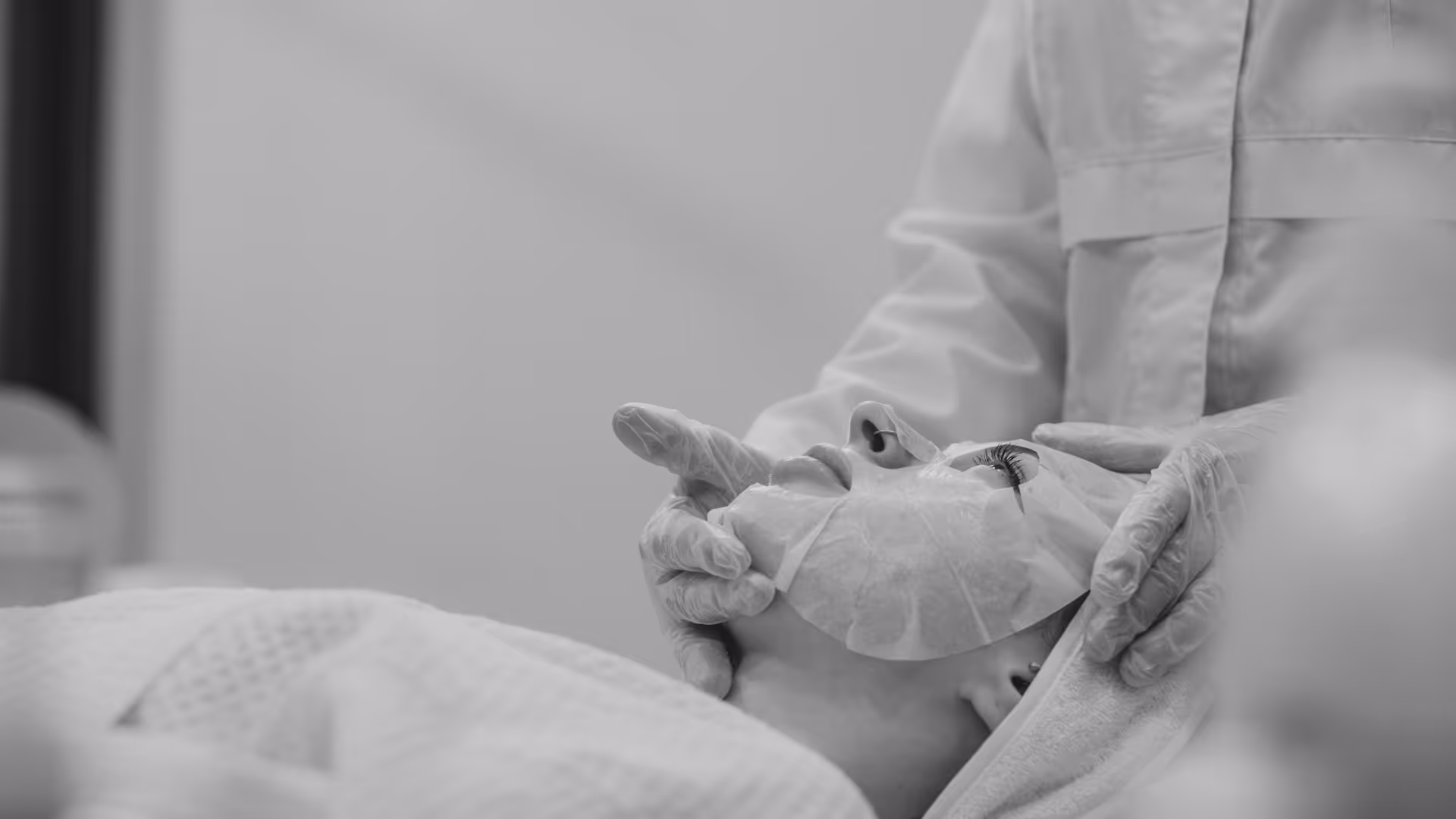 Cosmetologist applying mask on woman's face in spa salon