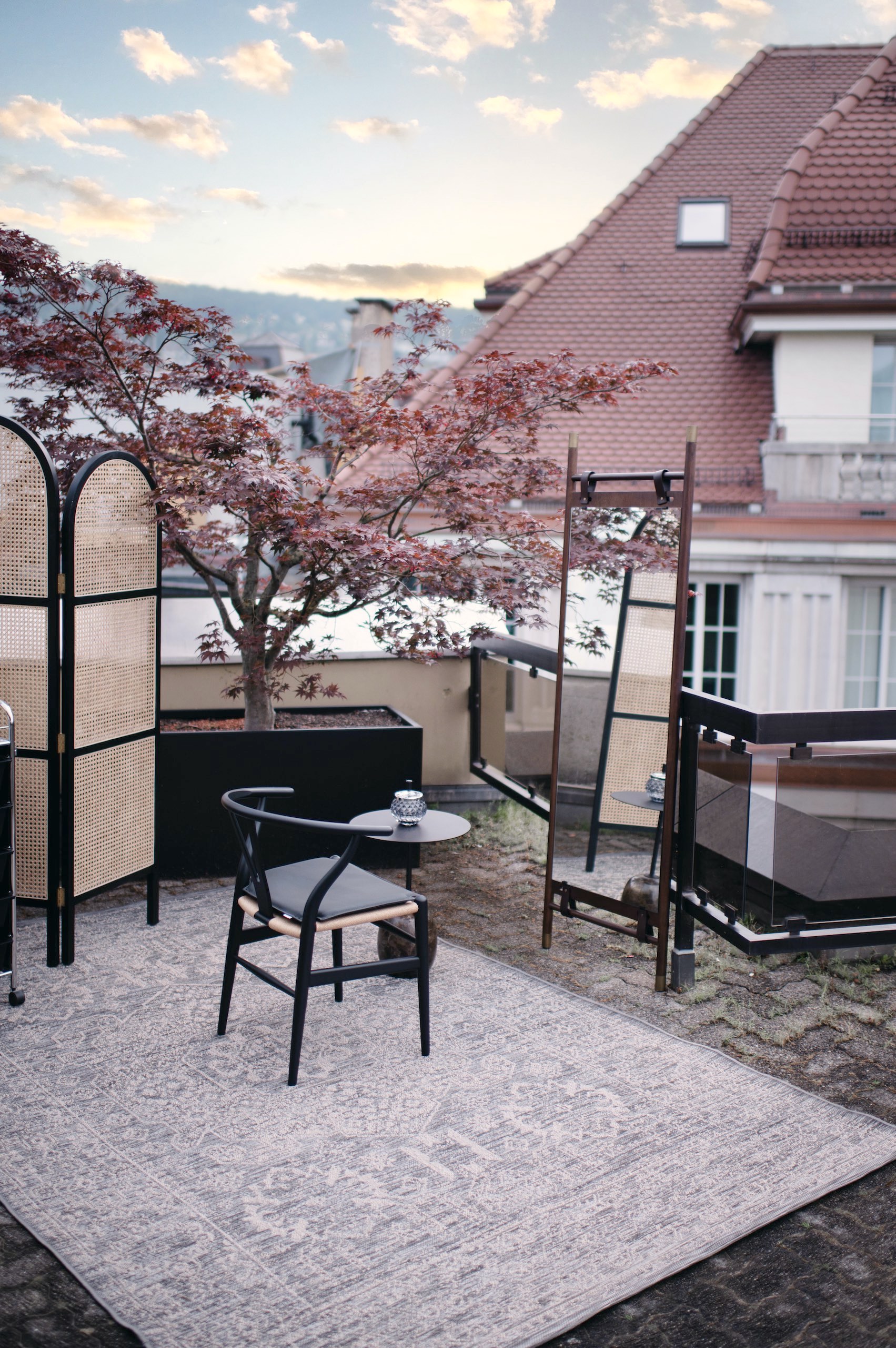 Outdoor terrace design showcasing vintage rug, mirror, and a black wishbone chair.