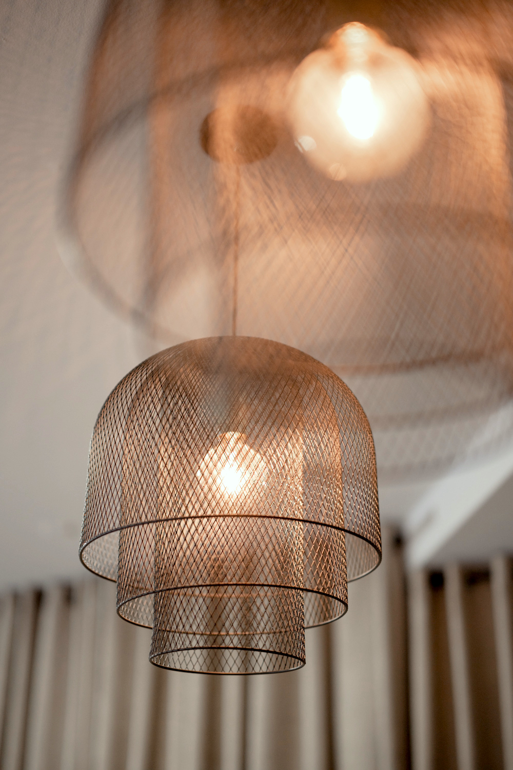 Two modern industrial-style pendant lamps with a beige curtain in the background.