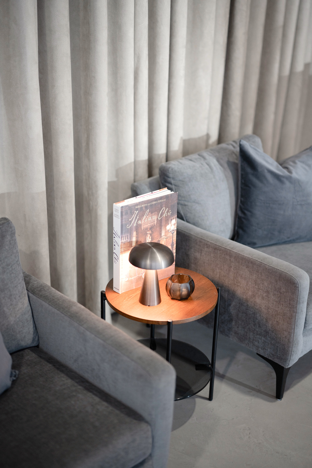 Two gray armchairs and a side table with a wooden top in front of a velvet curtain.