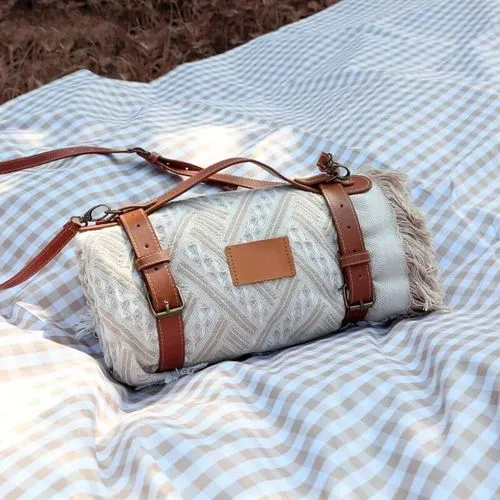 A picnic bag with leather straps on a picnic blanket
