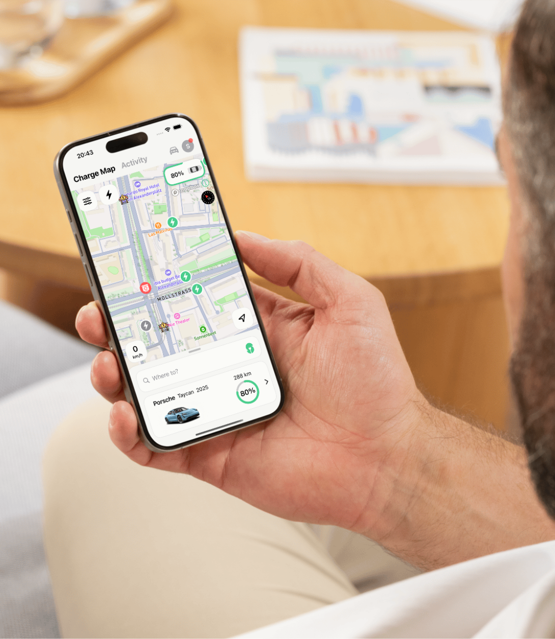Mann hält ein Smartphone mit einer Ladekarten-App, die Ladestationen und Ladestatus eines Porsche Taycan 2025 mit 80% Akku anzeigt.