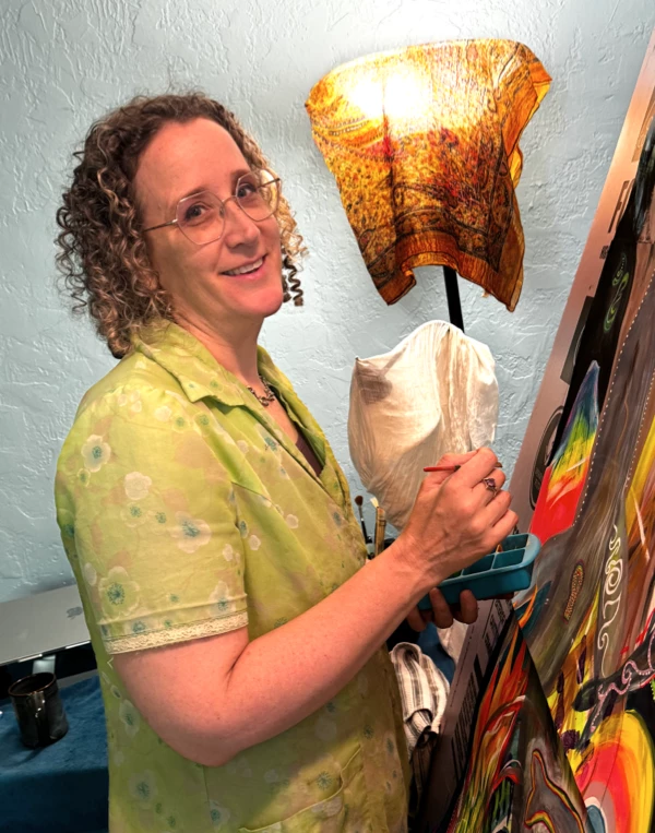 Jeannie standing at the painting easel, paints and brush in hand