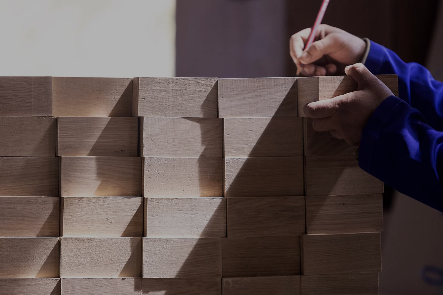 Person marking measurements on a wooden block wall with a pencil.