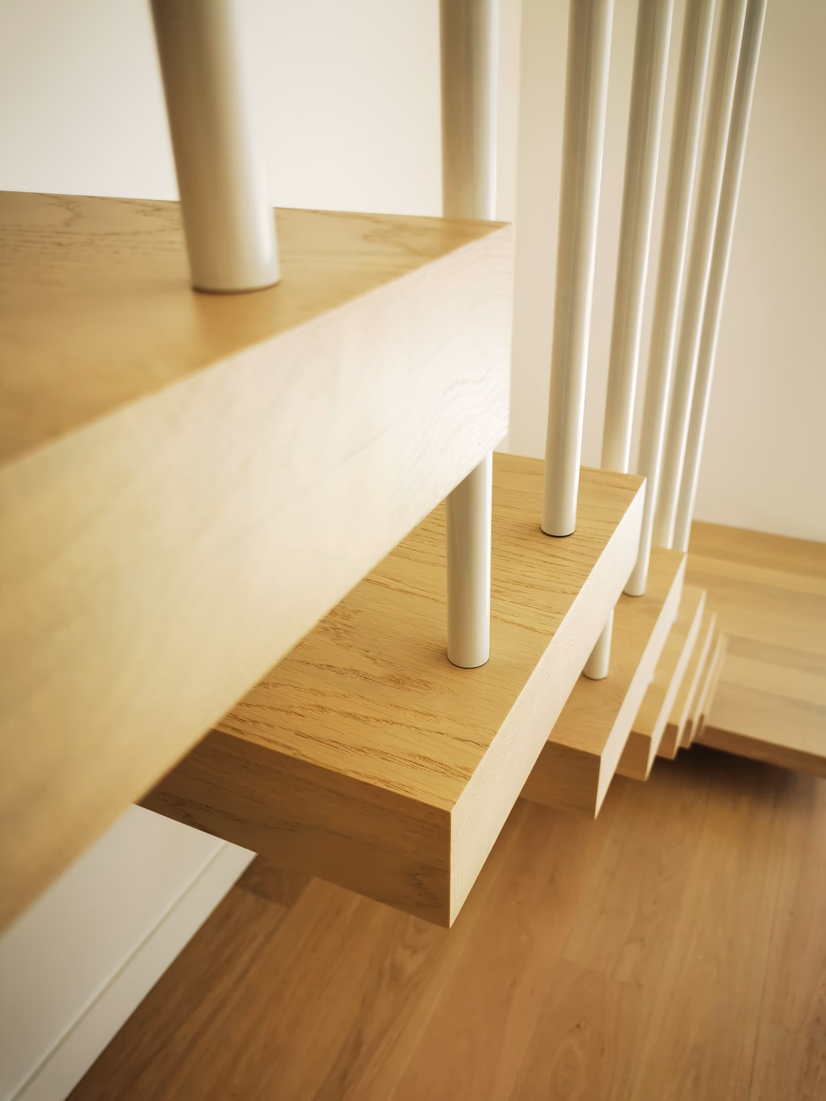 Close-up of modern wooden floating staircase steps with white cylindrical supports.