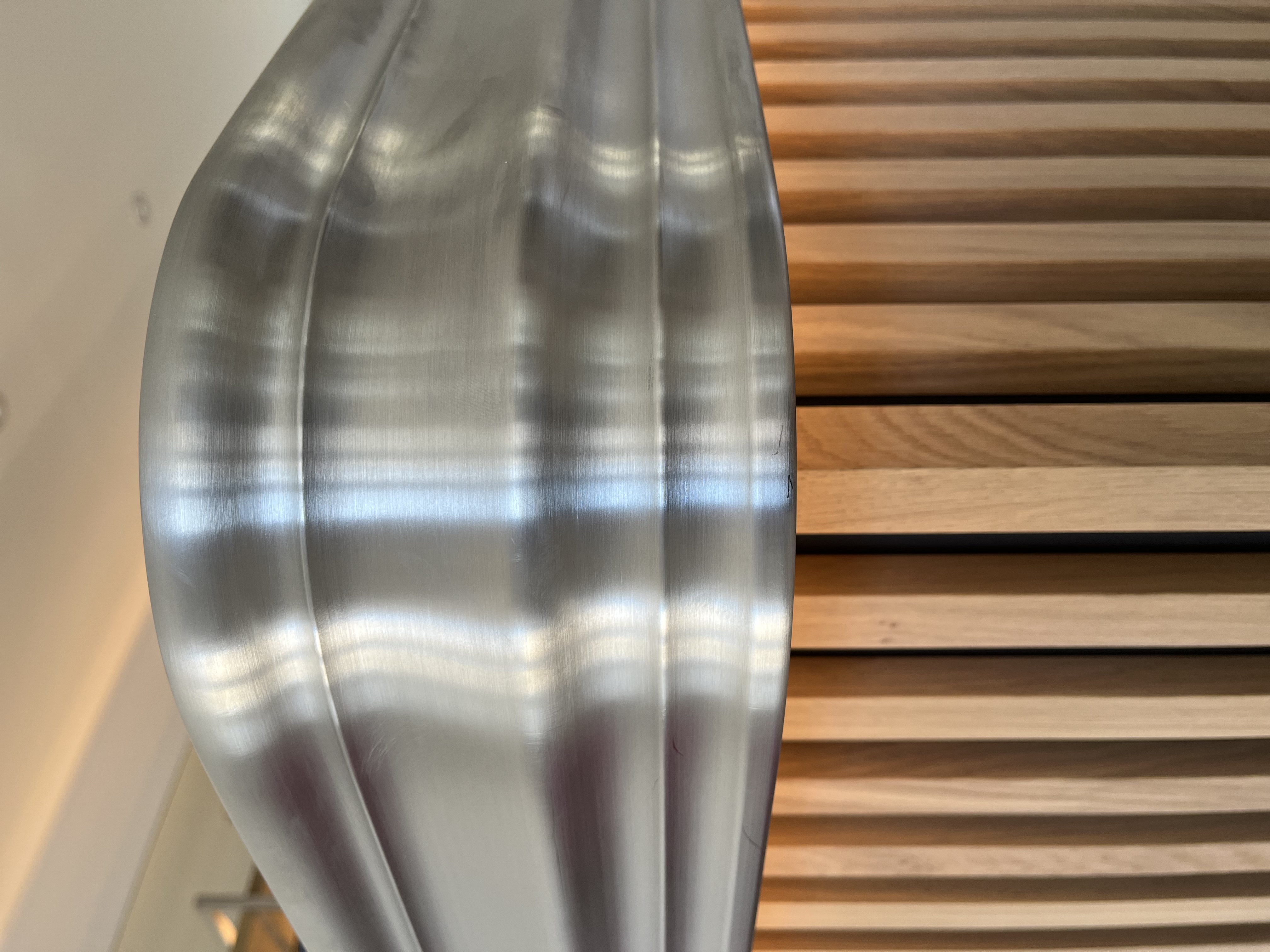 Close-up of a brushed metal object with reflective grooves above vertical wooden slats.