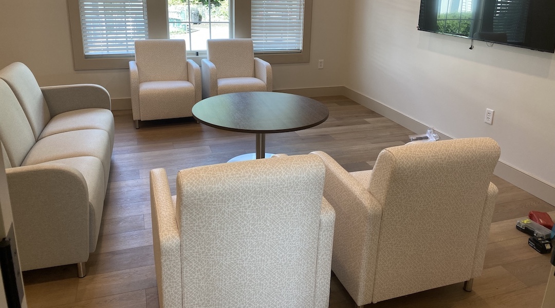 Cozy patient lounge in a treatment center with beige upholstered chairs, circular coffee table, and wall-mounted TV