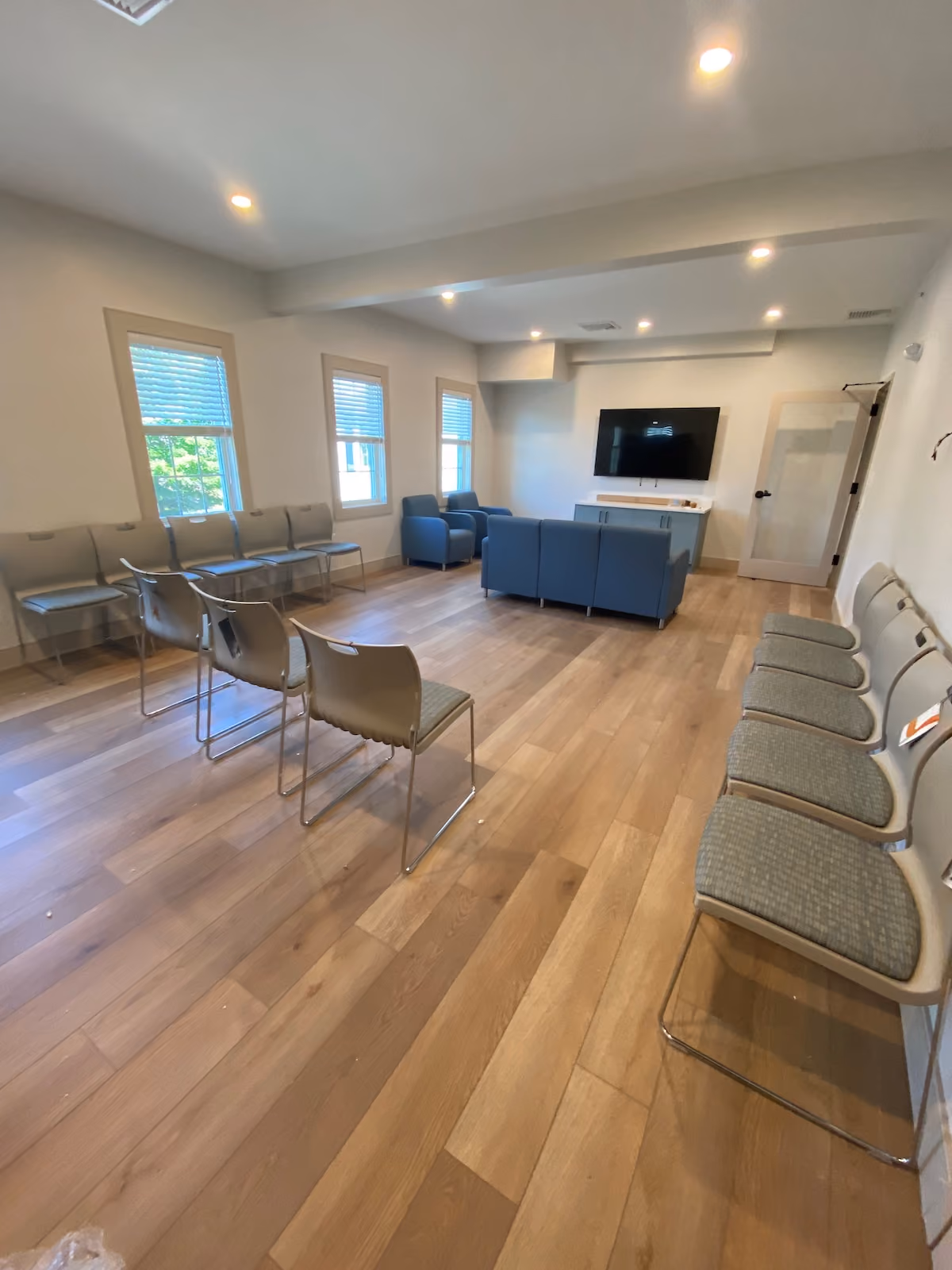 Residential treatment group room with multiple chairs, lounge seating, flat screen TV, and wood flooring for therapy sessions