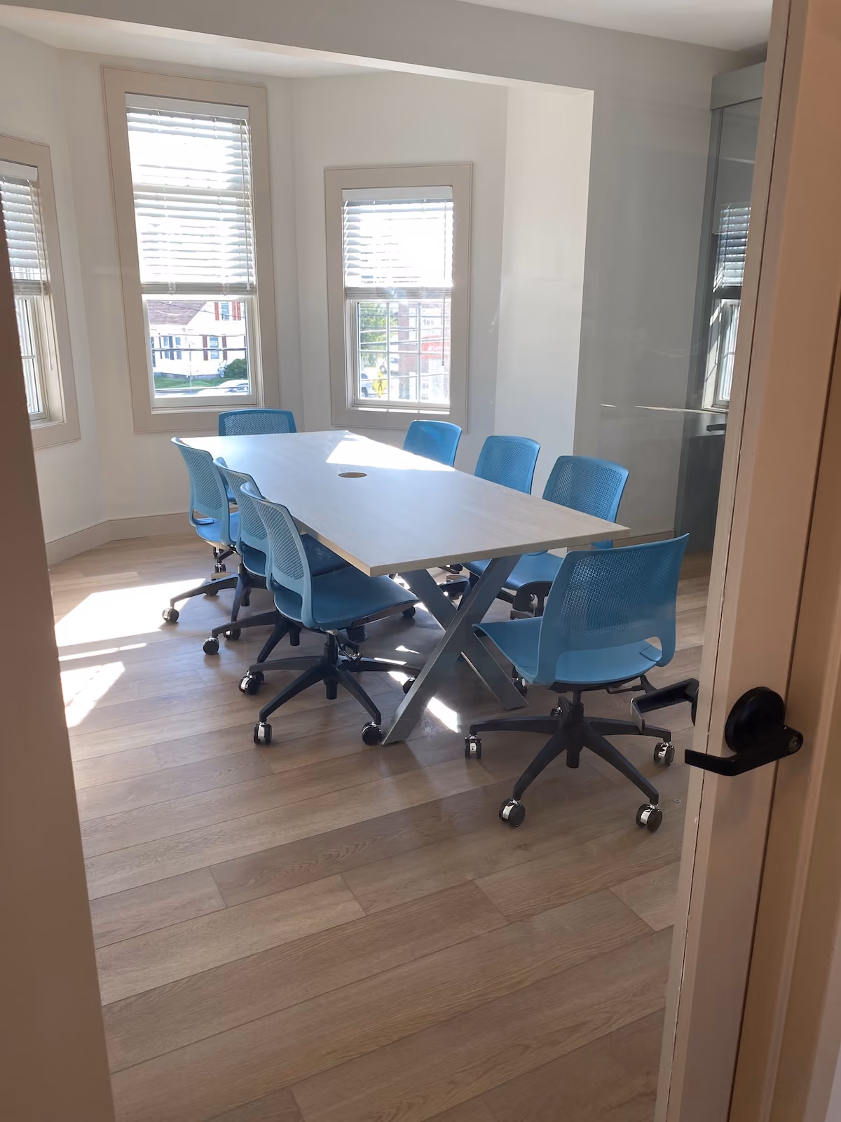 Modern treatment center conference room with large rectangular table, rolling blue chairs, and three tall windows with blinds